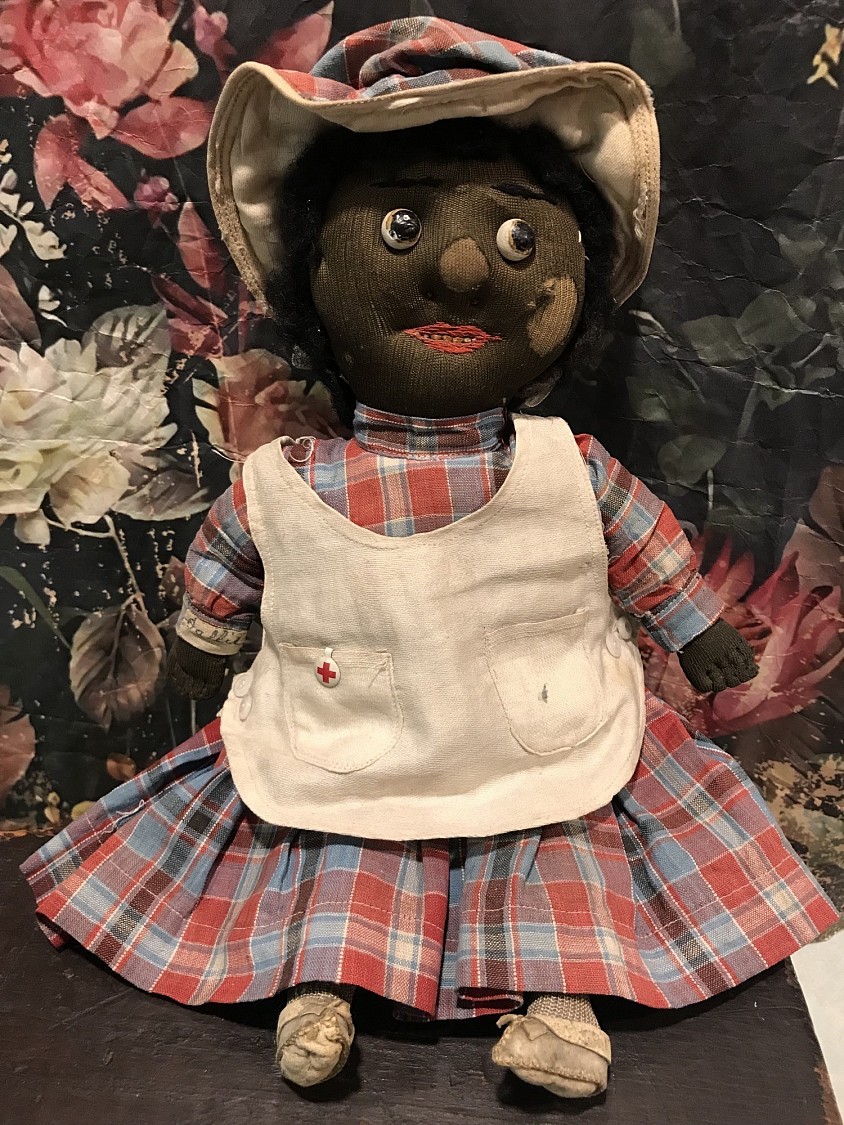Early black stockinette doll measuring 12.5” tall. She has such a sweet look. Her name is Sallie as the cloth name label that has been sewn onto her wrist confirms. She wears a colorful plaid dress with matching bonnet that has been sewn onto her head. Her early pinafore has 2 tiny milk glass buttons on each side and is the only piece of clothing not sewn onto her body. I LOVE the teeny metal Red Cross badge affixed to her pocket! Her face is quite unique having stitched brows, painted boot button eyes that glance to one side, red floss dots for nostrils and a smiling red floss mouth that shows her hand stitched teeth. My Favorite thing about her are her early socks and tiny very early leather shoes. She is an example of the ingenuity of a loving mama or grandma for a young girl. Sallie is a one of a kind early piece of Americana. She is sure to make you smile! 😀 ~ $ 295 postage paid within the US International buyers please contact me for shipping cost